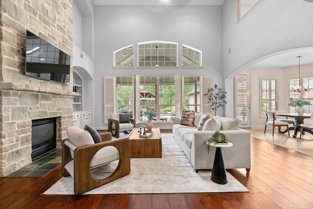 living room with a stone fireplace, a chandelier, wood-type flooring, and a high ceiling