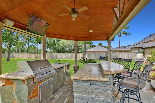 view of patio / terrace featuring ceiling fan, area for grilling, a wet bar, and exterior kitchen