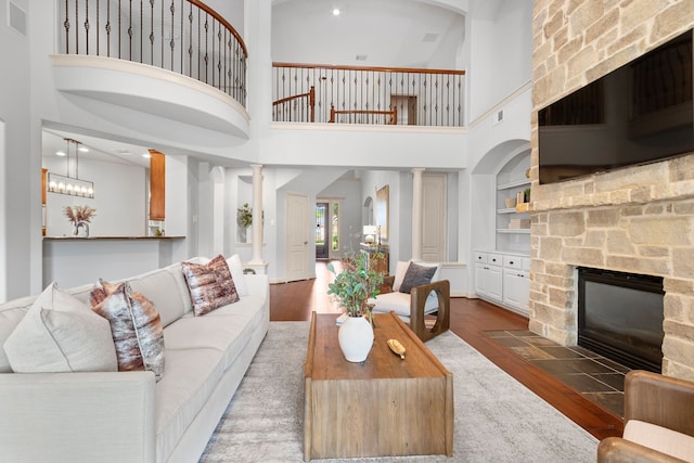 living room featuring a stone fireplace, built in features, dark hardwood / wood-style floors, and a towering ceiling