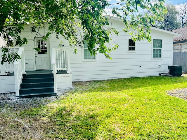 rear view of property featuring central air condition unit and a lawn