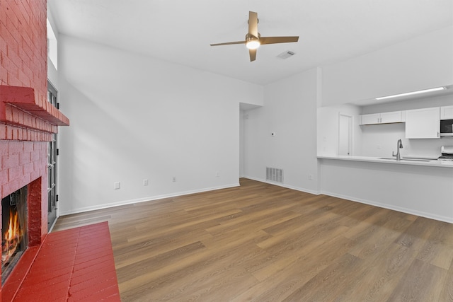 unfurnished living room featuring a brick fireplace, wood-type flooring, ceiling fan, and sink