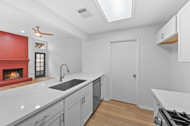 kitchen featuring a brick fireplace, stainless steel appliances, white cabinets, sink, and light wood-type flooring