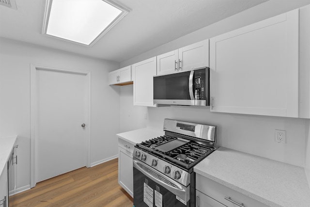 kitchen with light stone countertops, light hardwood / wood-style floors, white cabinetry, and appliances with stainless steel finishes