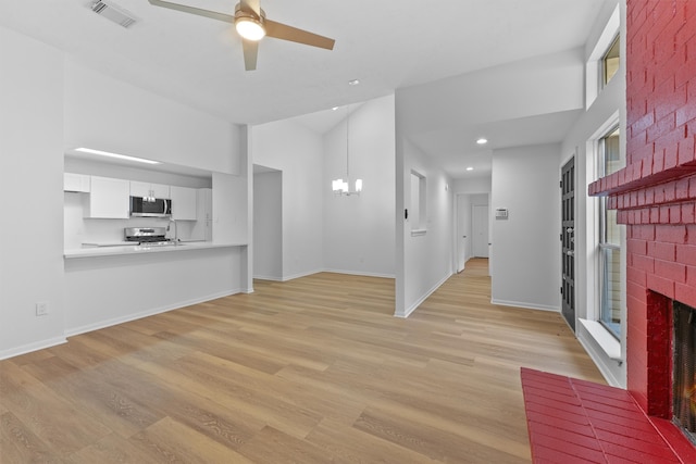 unfurnished living room with a brick fireplace, light hardwood / wood-style floors, and ceiling fan with notable chandelier