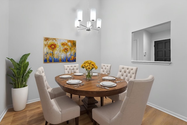 dining area with hardwood / wood-style floors, a towering ceiling, and an inviting chandelier