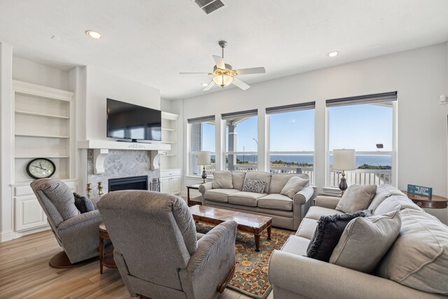 living room featuring a fireplace, ceiling fan, built in features, and light wood-type flooring