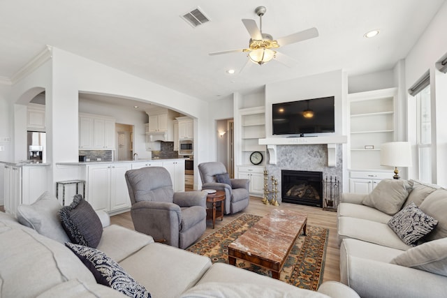 living room with light hardwood / wood-style floors, ceiling fan, a fireplace, crown molding, and built in features