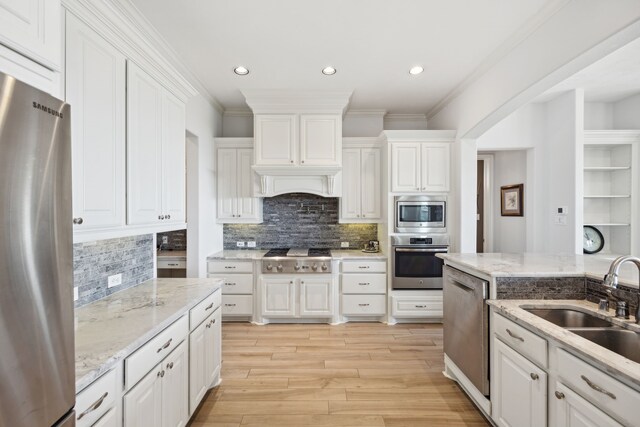 kitchen featuring tasteful backsplash, crown molding, white cabinetry, appliances with stainless steel finishes, and light wood-type flooring