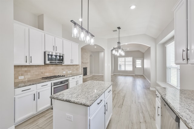 kitchen with white cabinets, appliances with stainless steel finishes, light stone counters, and a center island