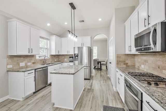 kitchen featuring light stone counters, a center island, stainless steel appliances, sink, and light hardwood / wood-style flooring