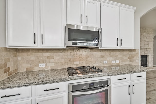 kitchen with white cabinetry, stainless steel appliances, tasteful backsplash, and light stone countertops