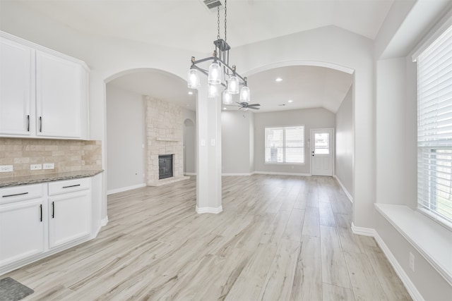 unfurnished living room featuring a stone fireplace, ceiling fan with notable chandelier, light hardwood / wood-style floors, and vaulted ceiling