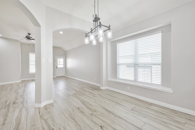 empty room featuring ceiling fan with notable chandelier, a wealth of natural light, lofted ceiling, and light hardwood / wood-style floors