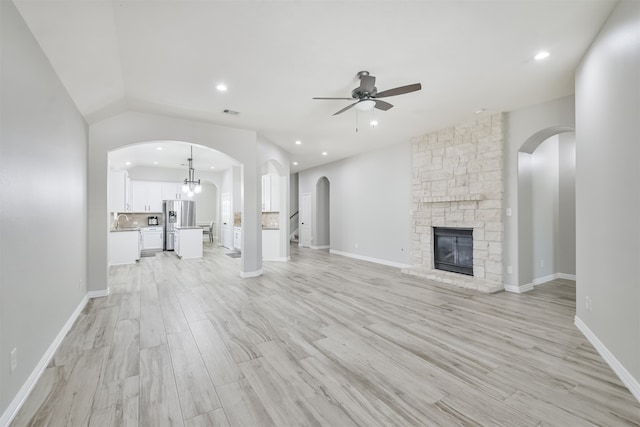 unfurnished living room with ceiling fan with notable chandelier, vaulted ceiling, light hardwood / wood-style floors, and a fireplace