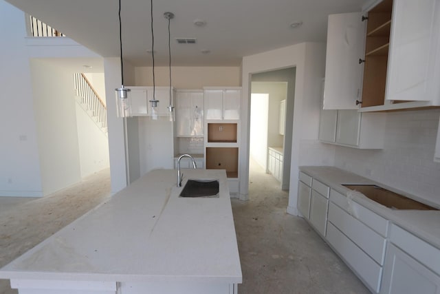 kitchen with pendant lighting, white cabinets, a sink, and an island with sink