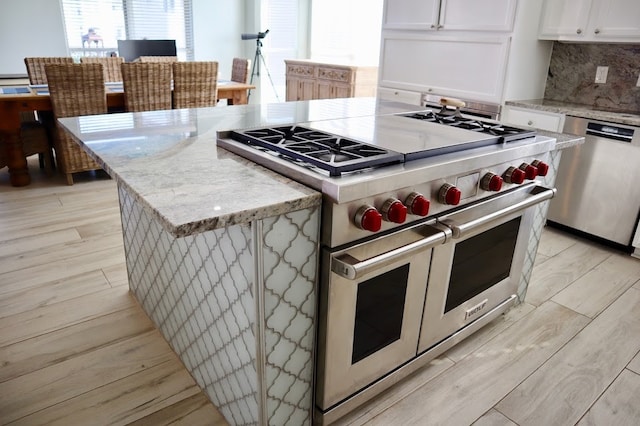 kitchen with white cabinets, appliances with stainless steel finishes, light hardwood / wood-style floors, and tasteful backsplash