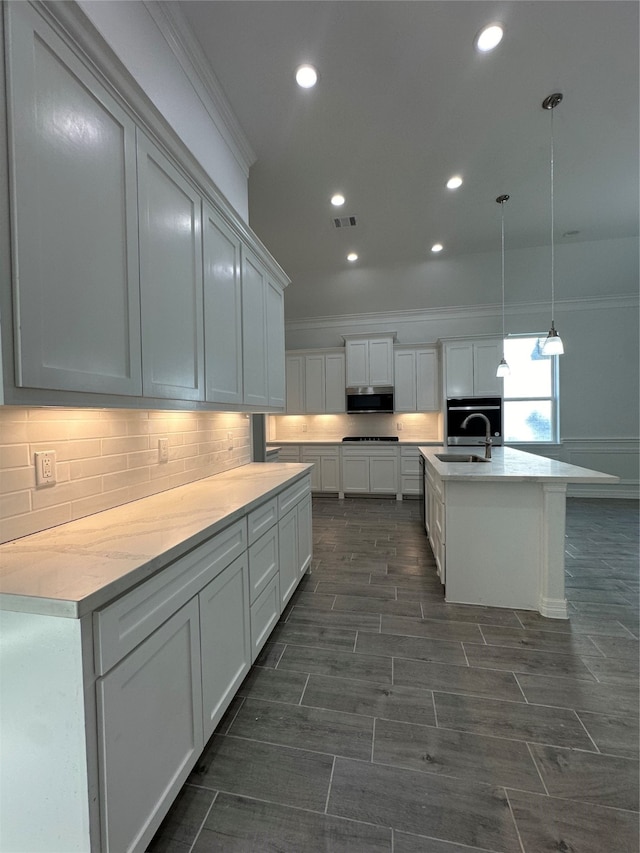 kitchen with ornamental molding, white cabinetry, decorative light fixtures, sink, and a kitchen island with sink