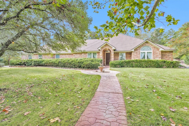 ranch-style house with a front lawn, roof with shingles, and brick siding