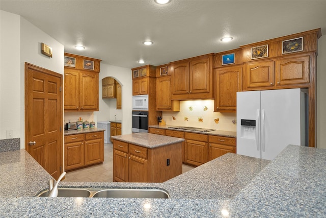 kitchen with brown cabinetry, arched walkways, white appliances, and a sink