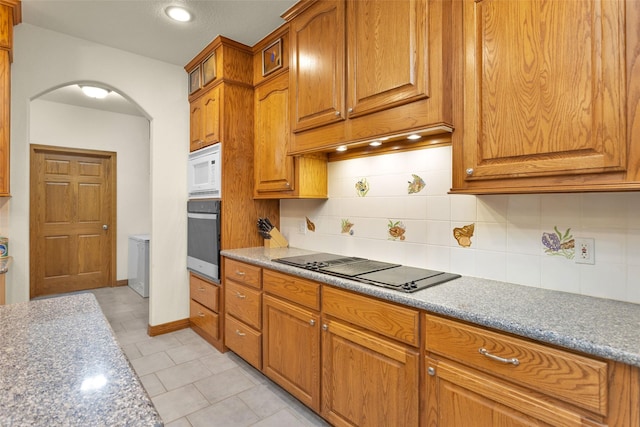 kitchen featuring arched walkways, black electric stovetop, backsplash, white microwave, and oven