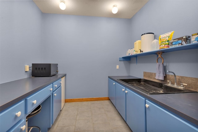 kitchen with blue cabinets, dark countertops, open shelves, and a sink