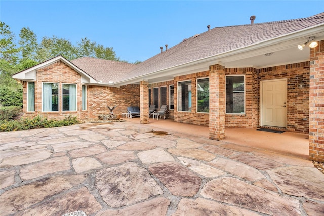 rear view of property featuring brick siding, roof with shingles, and a patio area