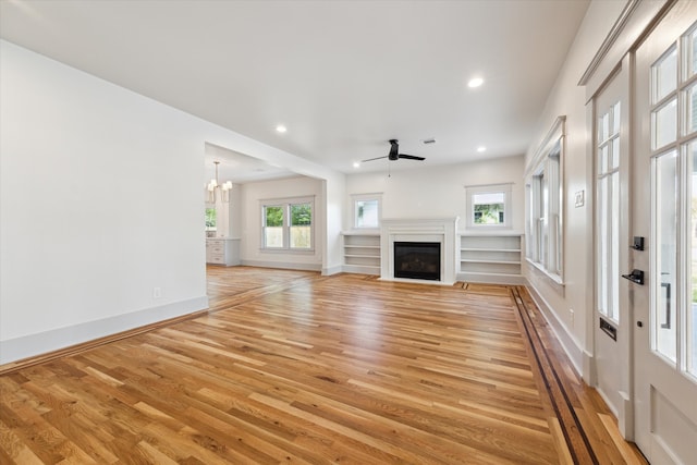 unfurnished living room with ceiling fan with notable chandelier and light wood-type flooring