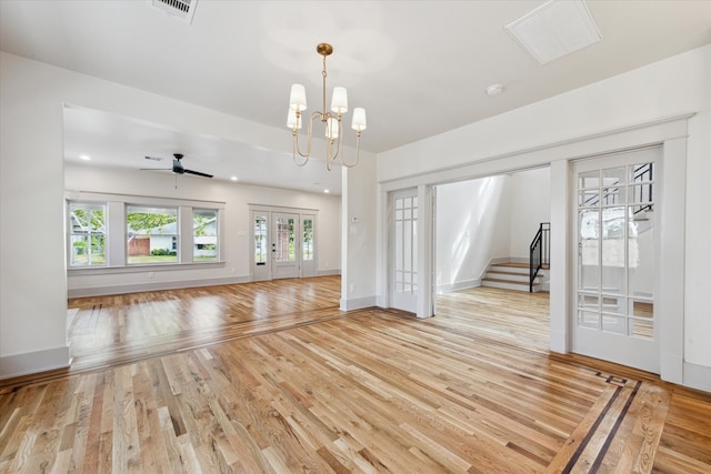 unfurnished living room with ceiling fan with notable chandelier and light hardwood / wood-style flooring