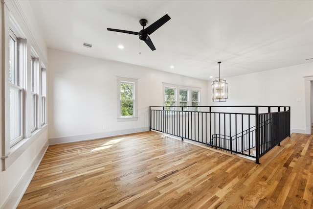 unfurnished room featuring ceiling fan with notable chandelier and light hardwood / wood-style flooring