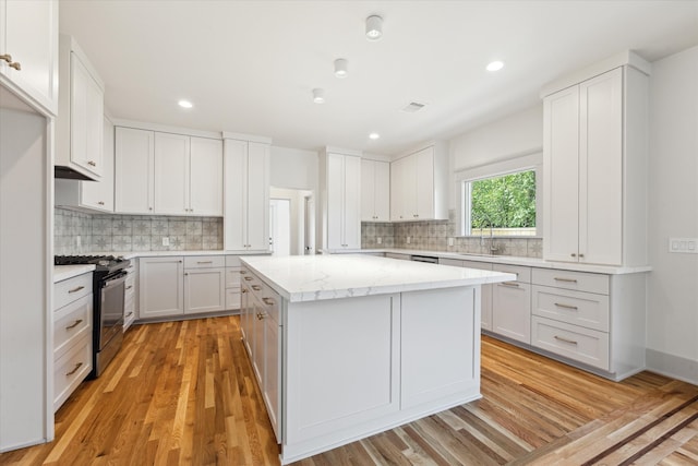 kitchen with stainless steel range with gas stovetop, sink, a kitchen island, white cabinets, and light wood-type flooring