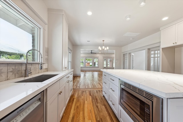 kitchen featuring light hardwood / wood-style flooring, sink, white cabinetry, appliances with stainless steel finishes, and decorative light fixtures