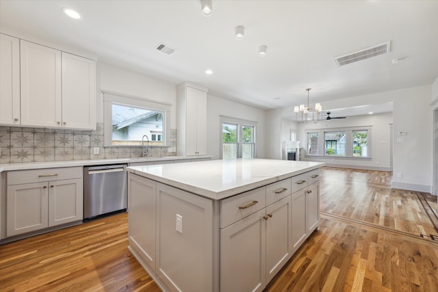 kitchen with stainless steel dishwasher, light wood-type flooring, a kitchen island, and tasteful backsplash