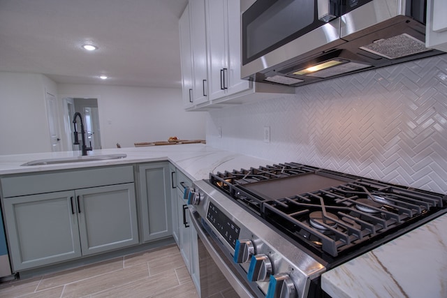 kitchen featuring stainless steel appliances, gray cabinets, light stone countertops, decorative backsplash, and sink