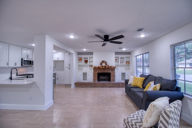 living room featuring sink, ceiling fan, light hardwood / wood-style flooring, a brick fireplace, and built in features