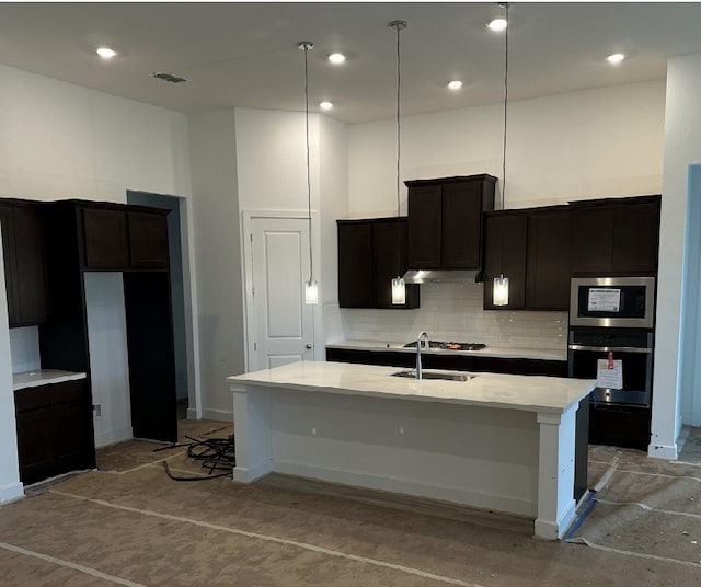 kitchen featuring oven, hanging light fixtures, a kitchen island with sink, built in microwave, and a high ceiling