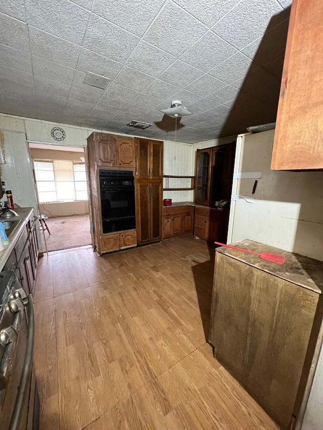 107 Thompson St, El Campo, TX 77437 - kitchen featuring black oven, brown cabinetry, a warming drawer, light wood-type flooring, and freestanding refrigerator