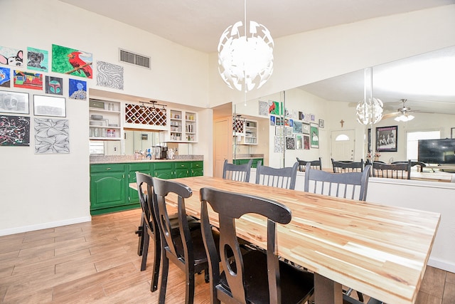 dining room with ceiling fan with notable chandelier, lofted ceiling, and light wood-type flooring