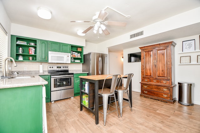 kitchen with stainless steel appliances, green cabinets, sink, backsplash, and light hardwood / wood-style flooring