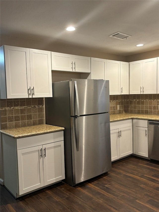 kitchen with light stone countertops, white cabinets, dark hardwood / wood-style floors, and appliances with stainless steel finishes