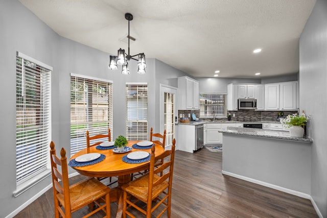 dining area with dark wood-type flooring, sink, a notable chandelier, and a textured ceiling