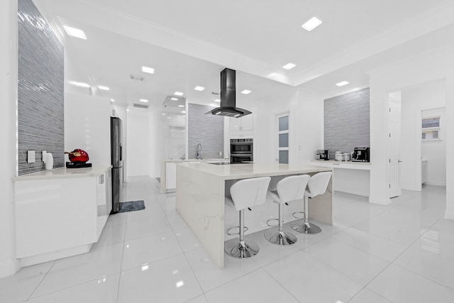 kitchen with white cabinets, fridge with ice dispenser, stainless steel double oven, a large island, and island exhaust hood