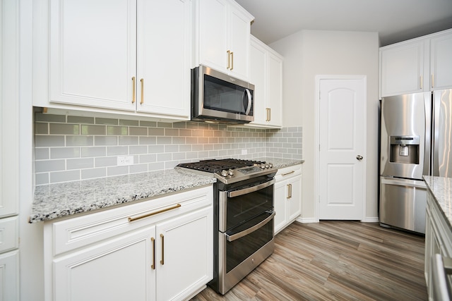 kitchen featuring light stone counters, backsplash, white cabinetry, light wood-type flooring, and appliances with stainless steel finishes