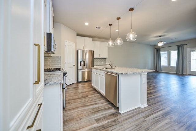 kitchen featuring light hardwood / wood-style floors, a center island with sink, white cabinets, tasteful backsplash, and appliances with stainless steel finishes