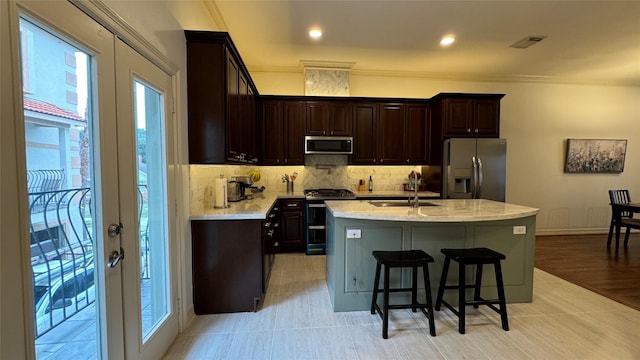 kitchen with appliances with stainless steel finishes, a kitchen island with sink, light stone counters, and french doors