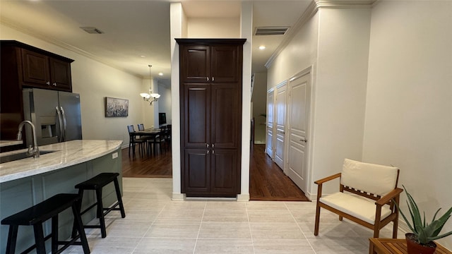 kitchen featuring a breakfast bar, sink, stainless steel fridge, a chandelier, and crown molding