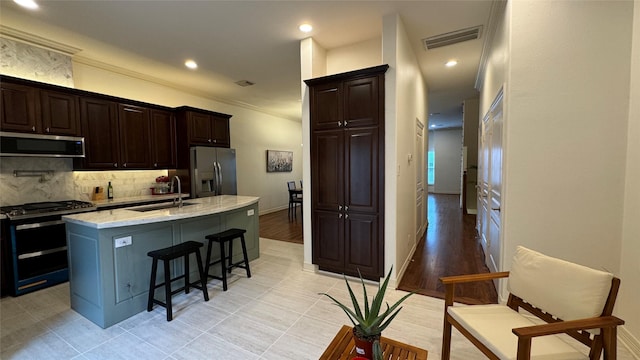 kitchen with sink, light stone counters, tasteful backsplash, a center island with sink, and appliances with stainless steel finishes