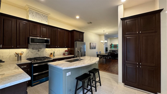 kitchen with appliances with stainless steel finishes, an island with sink, sink, a kitchen breakfast bar, and hanging light fixtures