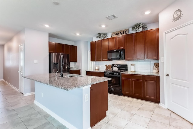 kitchen featuring backsplash, a kitchen island with sink, black appliances, sink, and light tile patterned floors