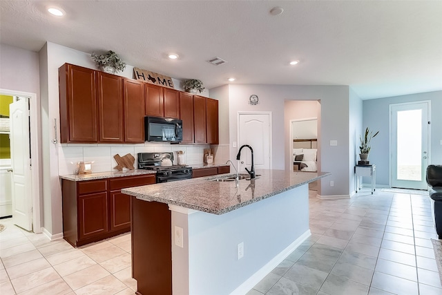 kitchen featuring black appliances, a center island with sink, sink, light tile patterned floors, and tasteful backsplash