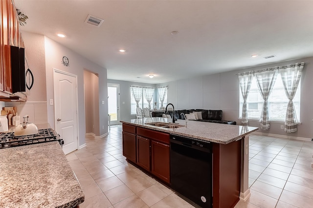 kitchen with light stone countertops, sink, black appliances, light tile patterned floors, and an island with sink